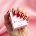 An extreme macro close-up, high-resolution image showcasing the precise architectural color photography of a hand with short, almond-shaped, deep ruby red press-on nails. The hand holds a soft pink Glamnetic nail b.webp