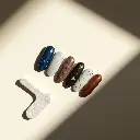 High contrast, low-key lighting, cinematic style flat lay of Heyhae Dreaming of You nail strips. Celestial designs deep blue, marble white, gold stars, earthy brown.  Mini file, prep pad, wooden stick. Cream backgr.webp