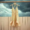 Dynamic motion in intense dramatic weather. A soft beige rayon, cotton, and sheer mesh halter mini dress with a deep V-neckline, tie-back straps, and ruffled polka-dot hem hangs on a rustic wood wall with coastal e.webp