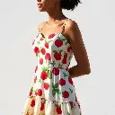 Candid street photography in natural earth tones a sleeveless ivory spaghetti strap sundress with a red strawberry and green leafy floral print against a white background.  The dress features a sweetheart neckline,.webp