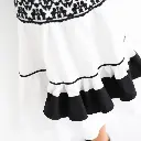 Close-up shot of a sleeveless white cotton poplin dress with black embroidered yoke, fabric belt, and ruffle tiers, on a white background.  Fit-and-flare silhouette, round neckline, styled with black ankle-strap he.webp