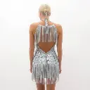 A shiny silver fringe mini dress, halter neck and backless style, displayed on a white backdrop within a thick fog. Low visibility, electric vivid colors.webp