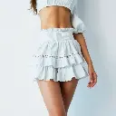 High-resolution product photo white double-layered ruffle mini skirt with lace trim and elastic waistband, built-in shorts. Woman with fair skin, wearing a cropped puff-sleeve blouse, poses against a white backgrou.webp