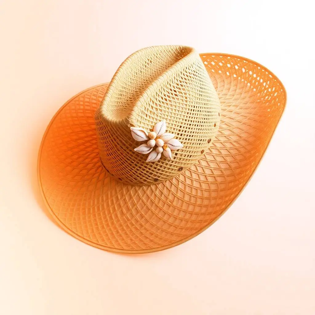 A smooth gradient transition of warm candlelight colors illuminates a beige straw cowgirl hat with a shapeable wide brim, open weave pattern, and decorative seashell trim band, photographed against a white backgrou.webp